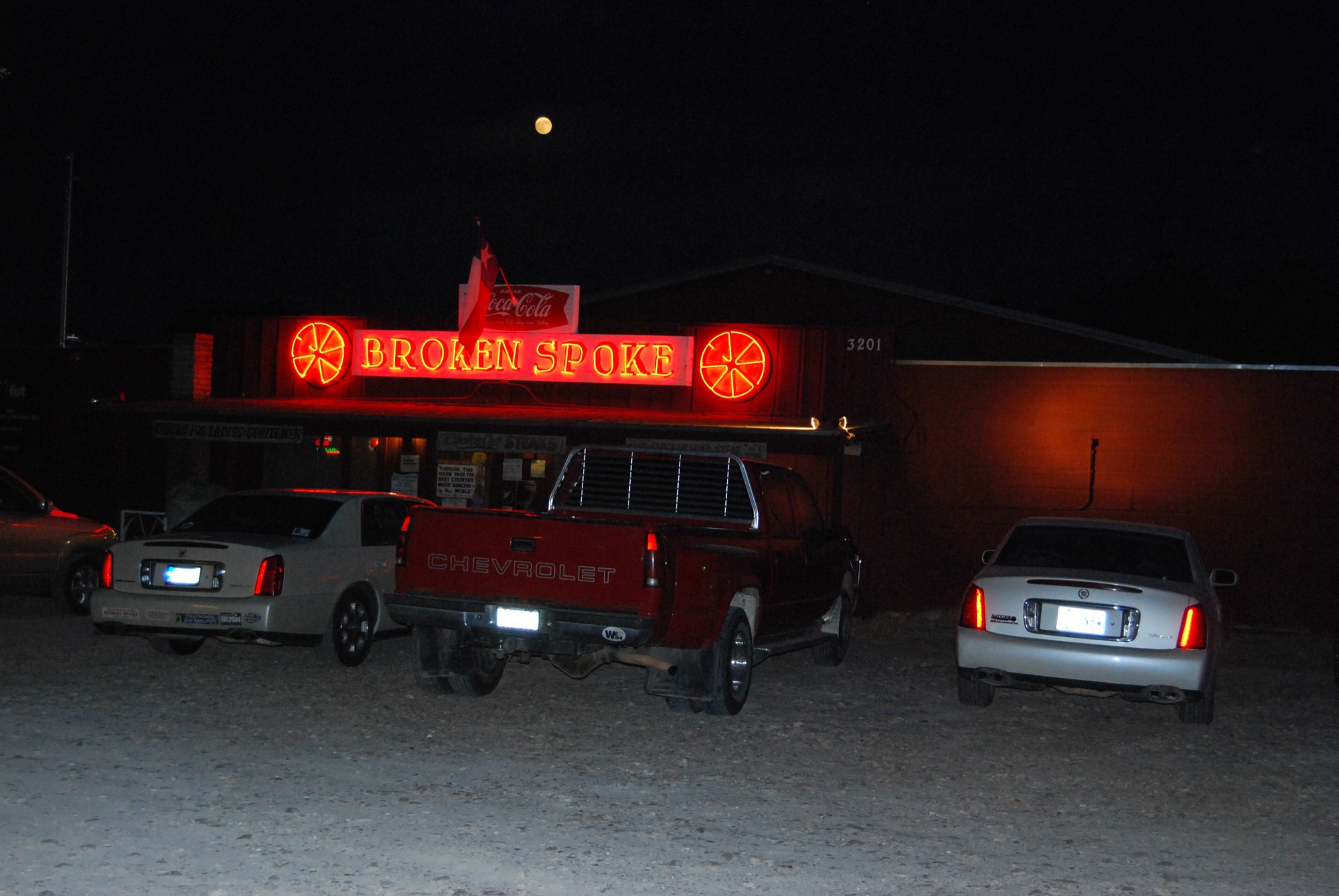 The Broken Spoke at night, its red neon sign glowing over the gravel lot