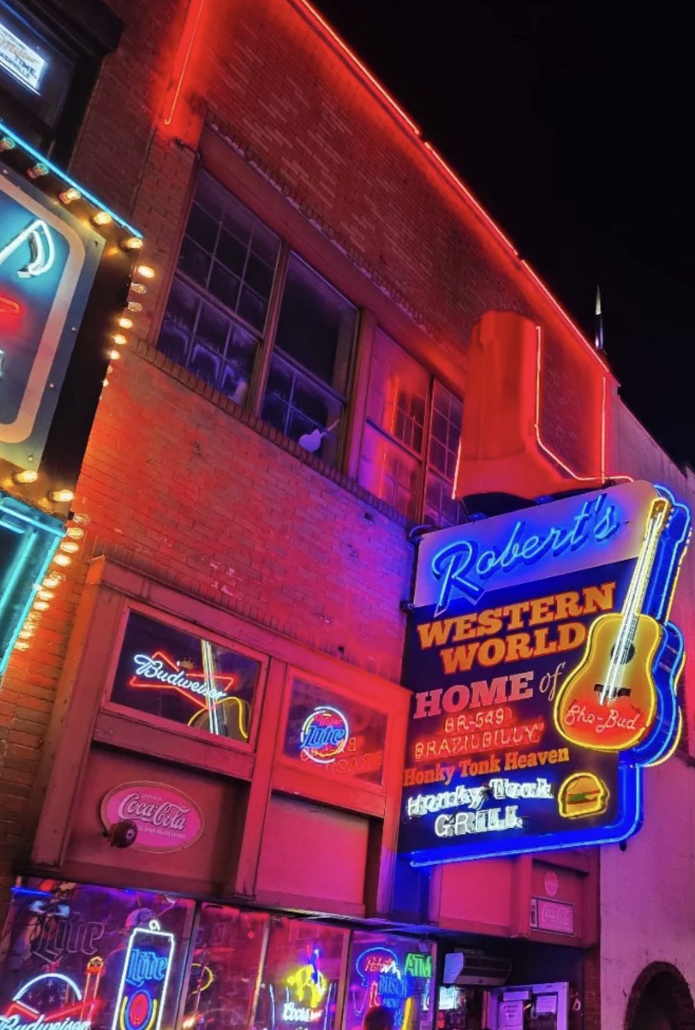 Robert's Western World at night: the red brick building outlined in red neon, the giant boot, and the blue-outlined sign with the Sho-Bud guitar